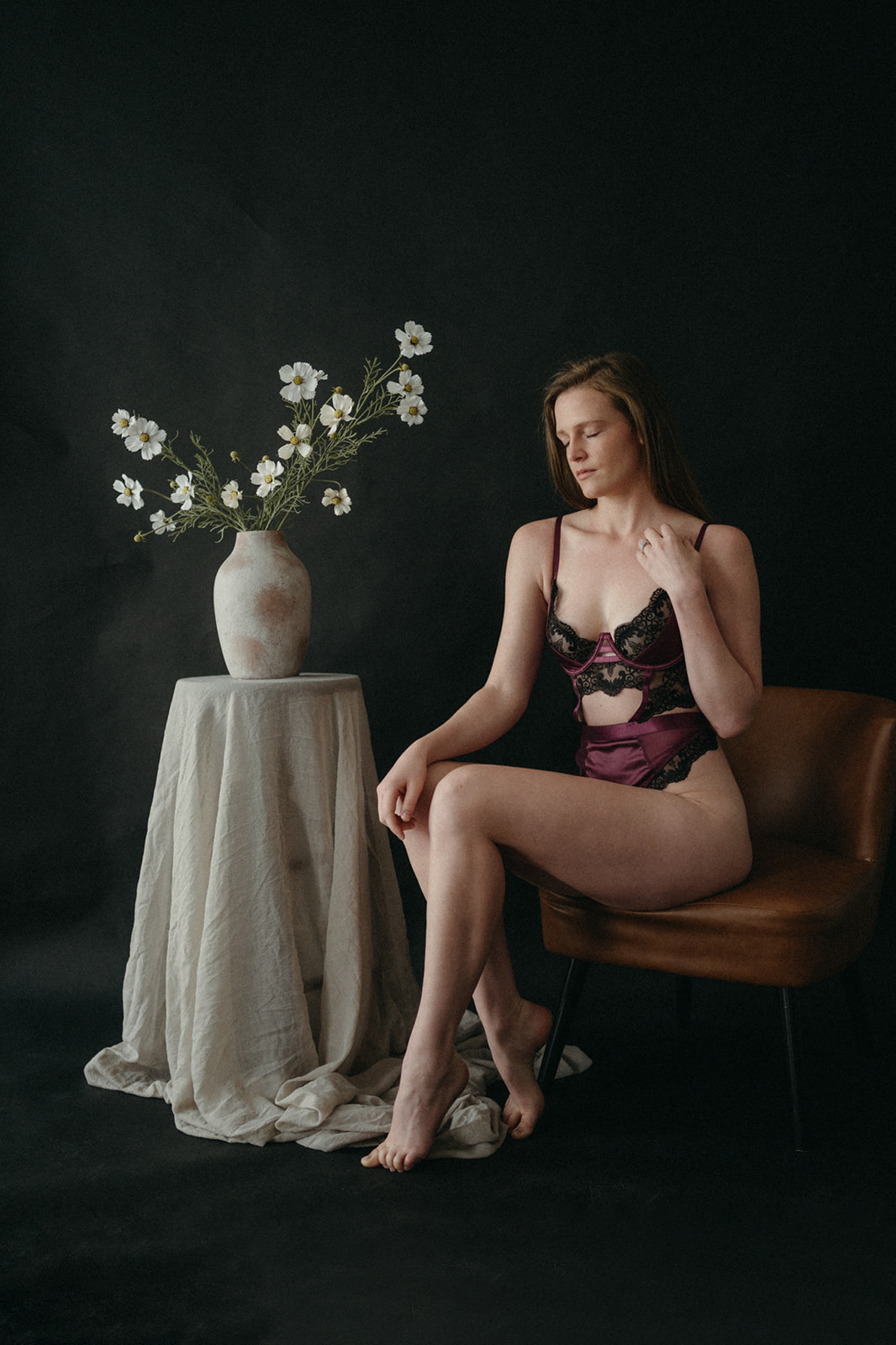 woman in maroon Apex Lingerie set sitting next to a table of greenery