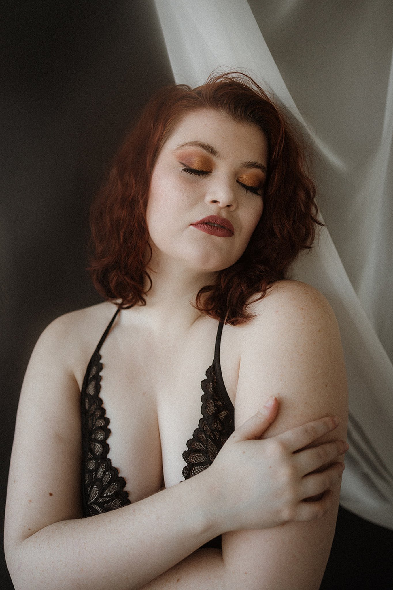 woman with red hair and lace lingerie hugging herself