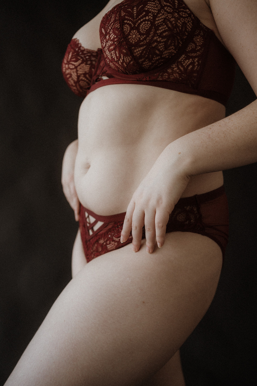 A woman wearing red Serasana lingerie stands with hands on her hips in a studio